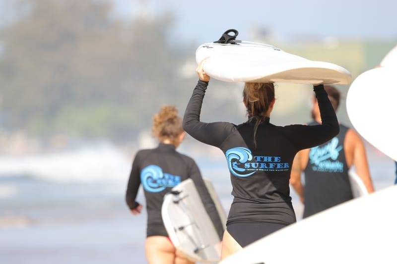 Guests in The Surfer rash guards carrying surfboards down to Weligama Bay, Sri Lanka
